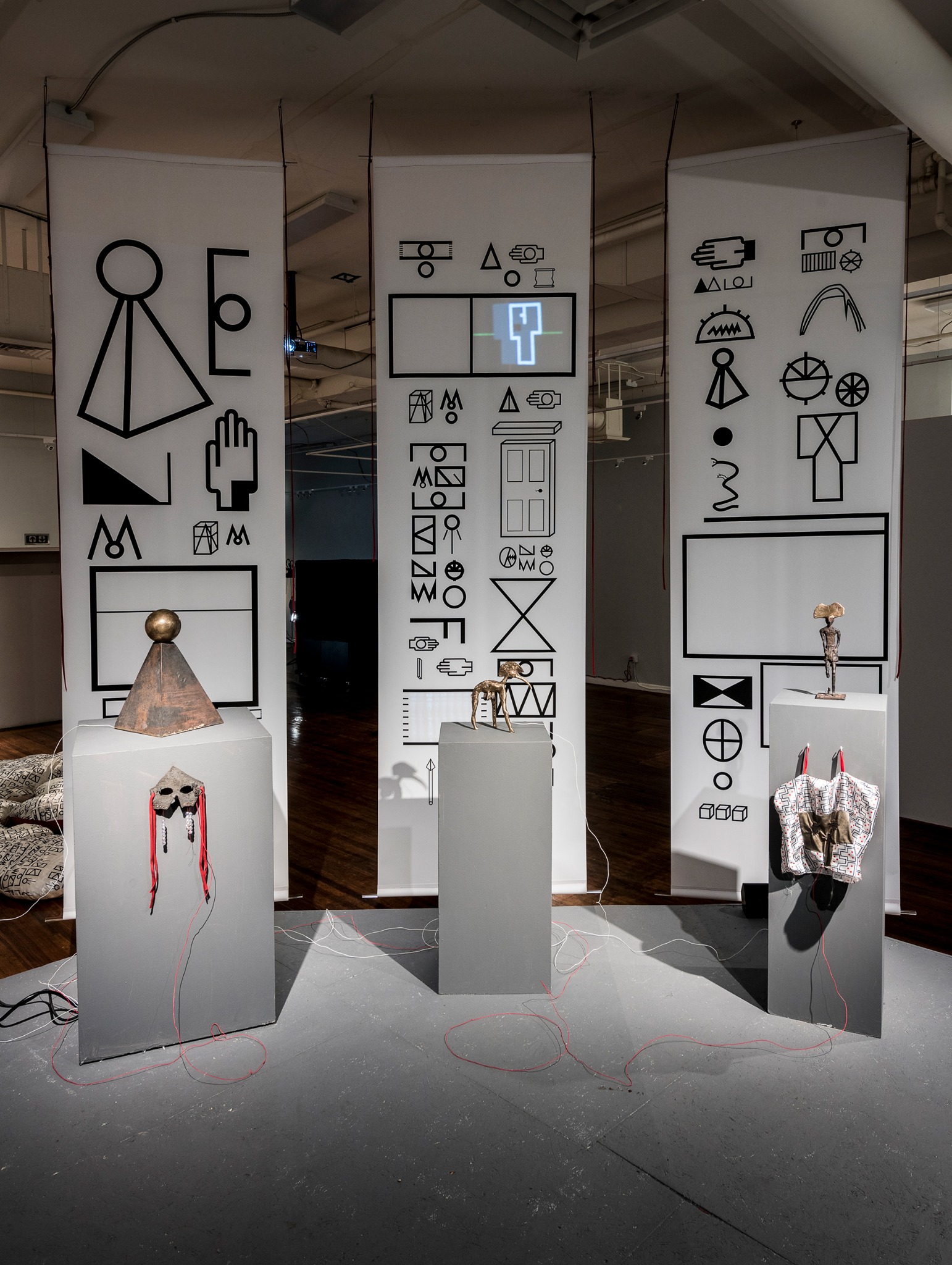 Acculturation Machine installation with bronze sculptures, pedestals, hanging graphic panels, wires, and projected images