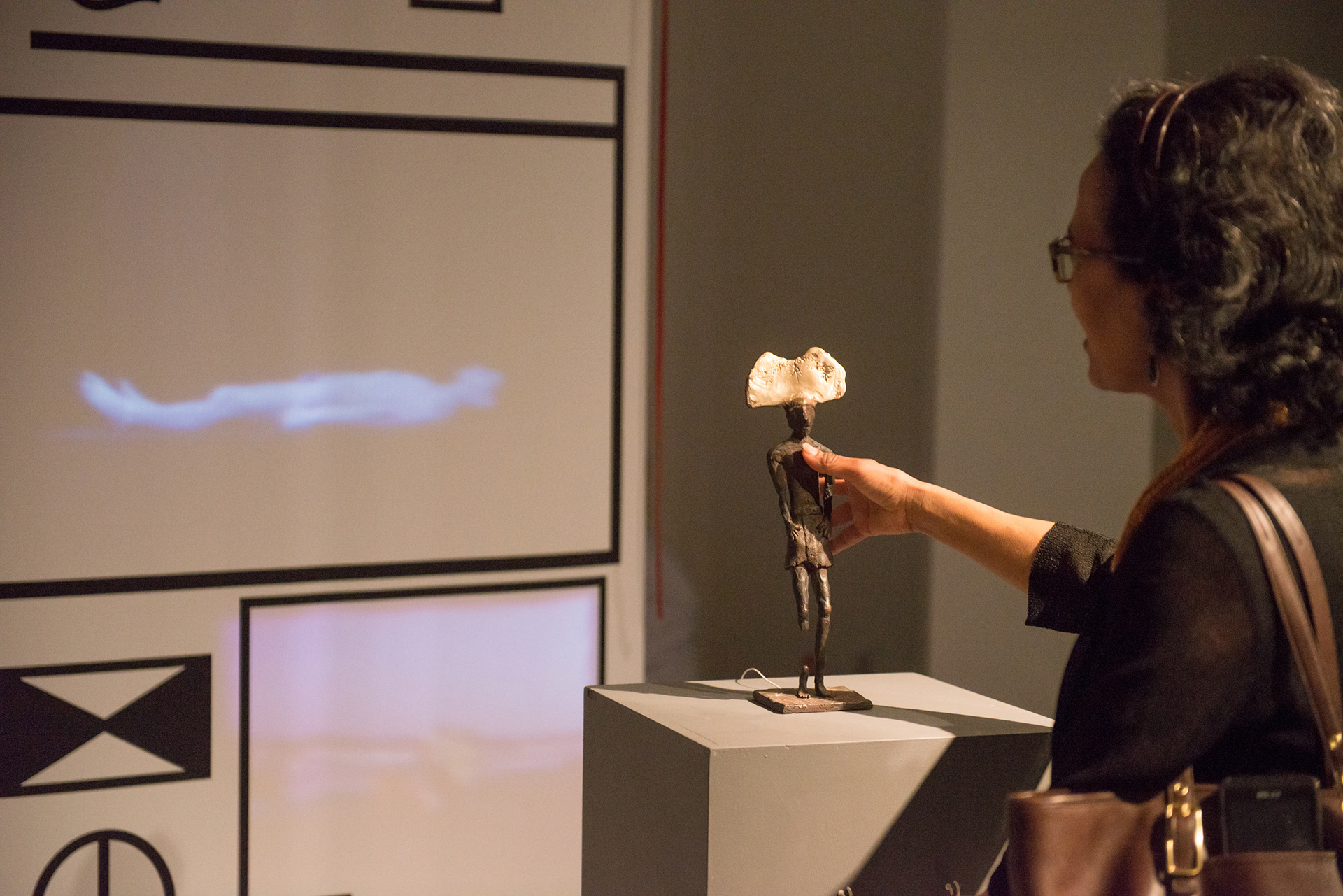Gallery visitor touching a bronze sculpture in Acculturation Machine