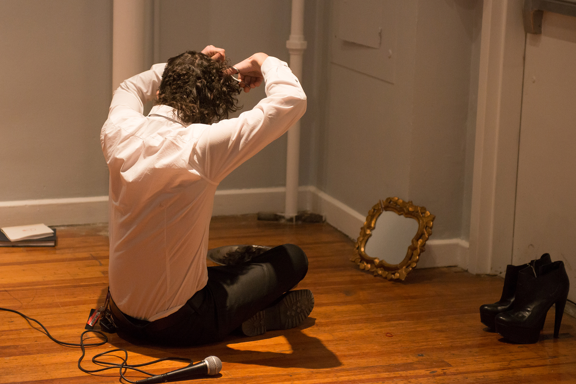 Performance view of the artist sitting on the gallery floor and cutting his hair