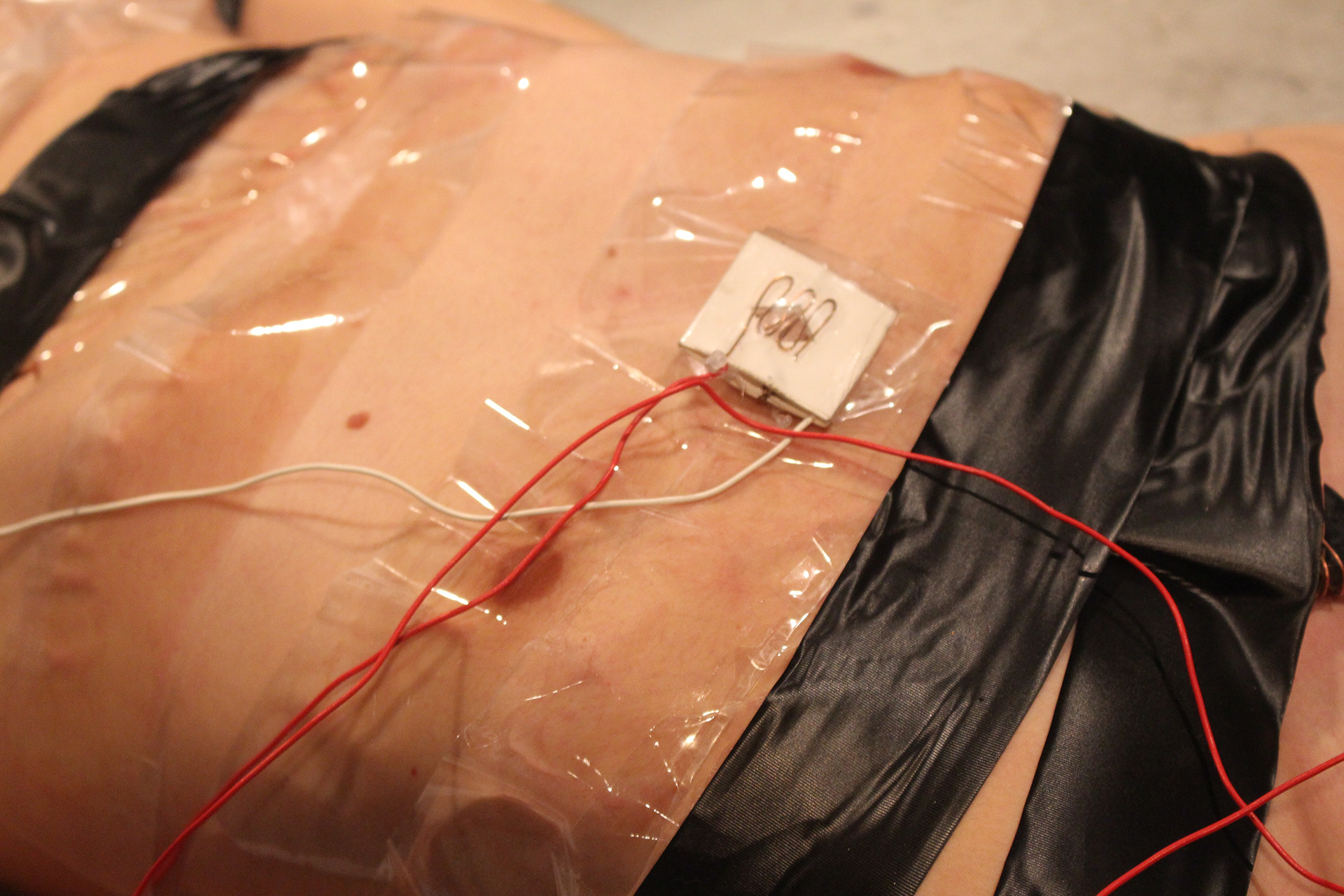 Close-up of a handmade sensor attached to the artist's chest with clear and black tape