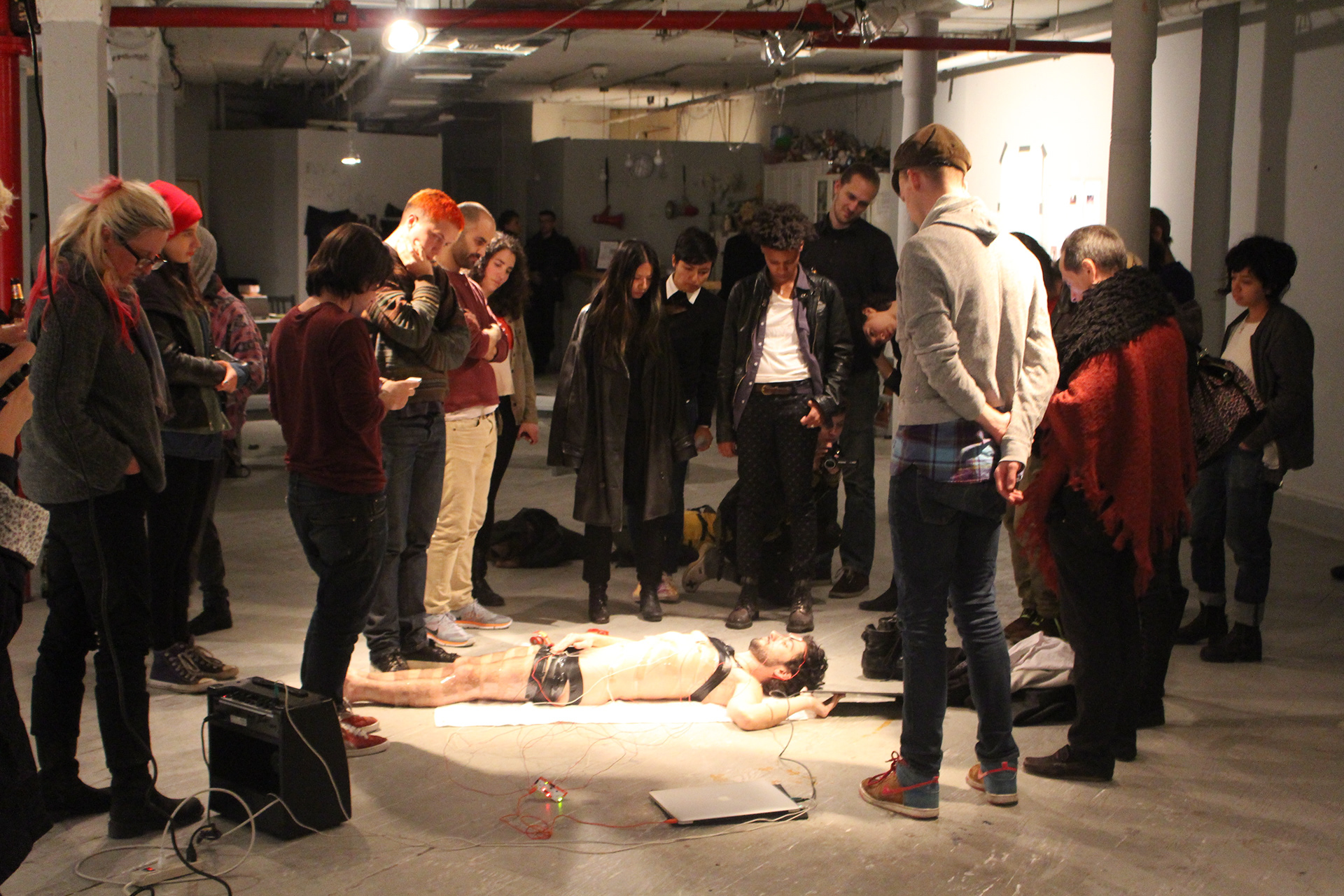 Audience members standing around the artist lying on the gallery floor