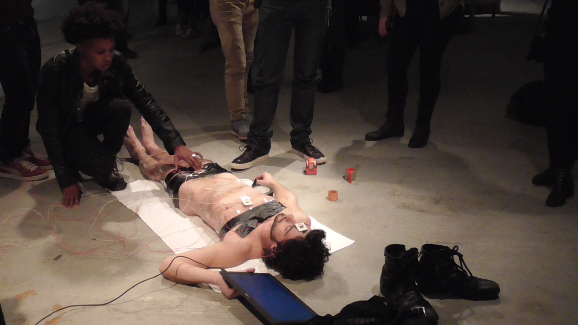 The artist lying on the gallery floor surrounded by wires and participants
